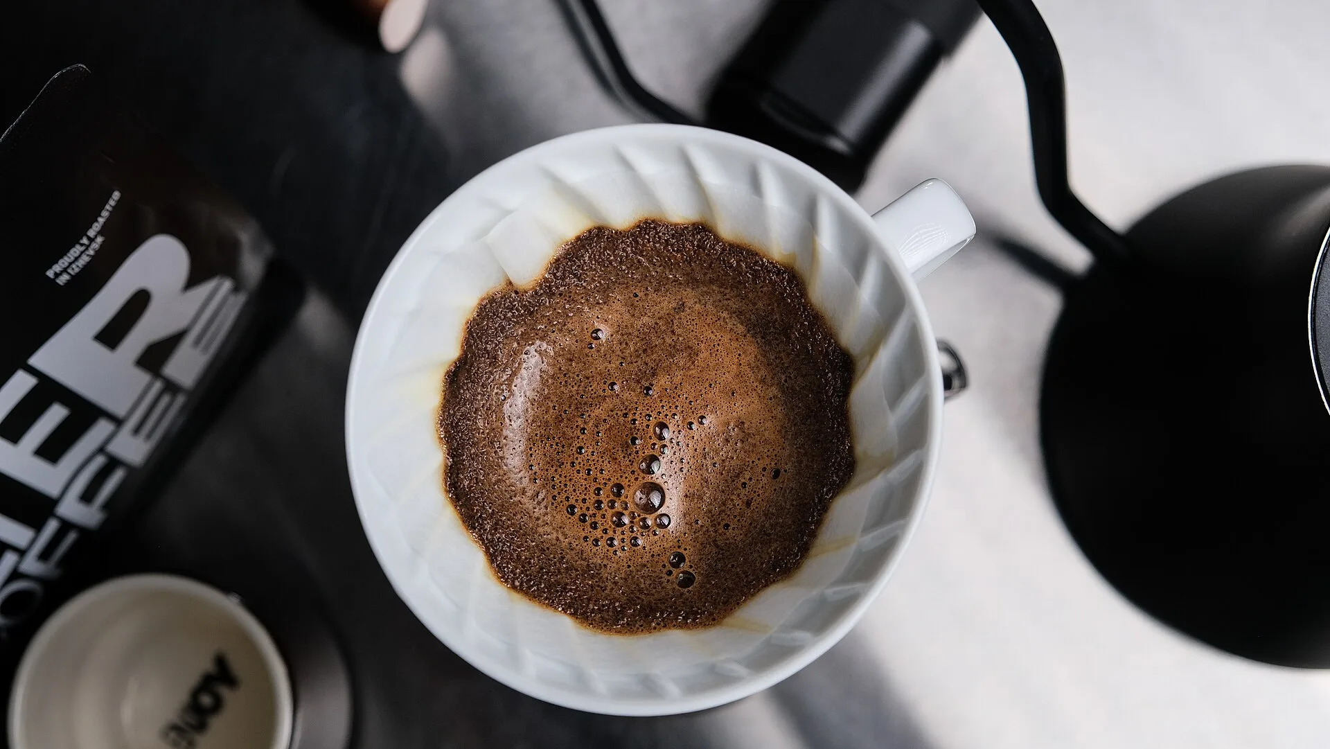 1=Freshly roasted coffee being brewed in a V60 pour-over dripper (bloom stage), close-up. Inside pour over: bloom, first pour, and drawdown at each brewing stage